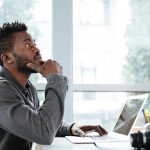 A professional sitting thoughtfully at a laptop in a coworking space, reflecting on how modern work turns social interaction into opportunity.