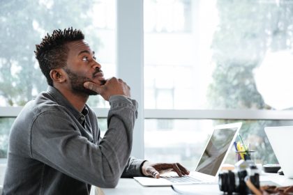 A professional sitting thoughtfully at a laptop in a coworking space, reflecting on how modern work turns social interaction into opportunity.