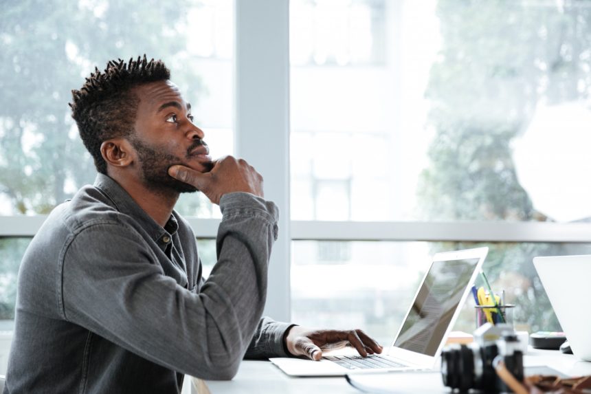 A professional sitting thoughtfully at a laptop in a coworking space, reflecting on how modern work turns social interaction into opportunity.