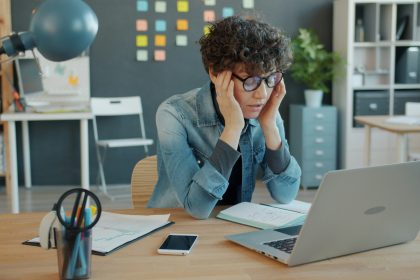 A stressed office worker at a desk with a laptop, showing signs of mental fatigue and burnout.