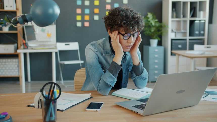 A stressed office worker at a desk with a laptop, showing signs of mental fatigue and burnout.