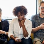 A diverse group of commuters on a train, each absorbed in their smartphones