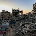 Bombed-out residential buildings stand gutted against a warm sunset sky, with rubble and makeshift shelters filling the foreground, a scene of civilisational collapse in the midst of lingering beauty.