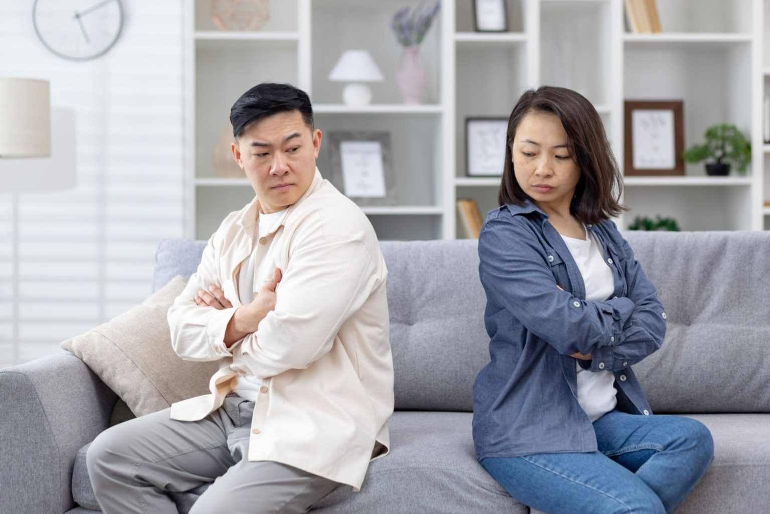 A couple sitting back to back on a sofa with arms crossed, showing emotional distance and lack of communication.