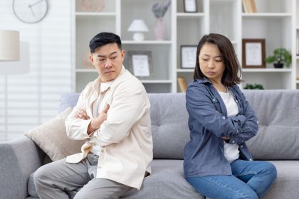 A couple sitting back to back on a sofa with arms crossed, showing emotional distance and lack of communication.