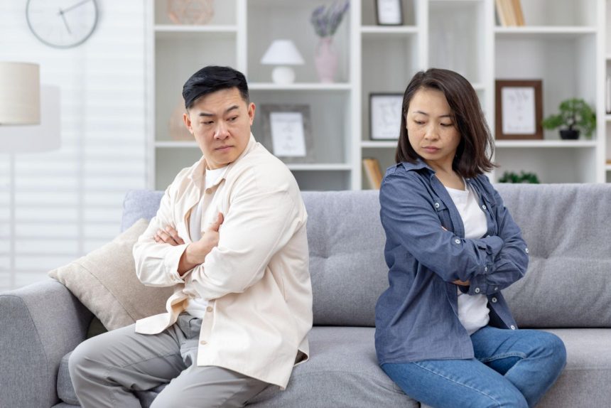 A couple sitting back to back on a sofa with arms crossed, showing emotional distance and lack of communication.